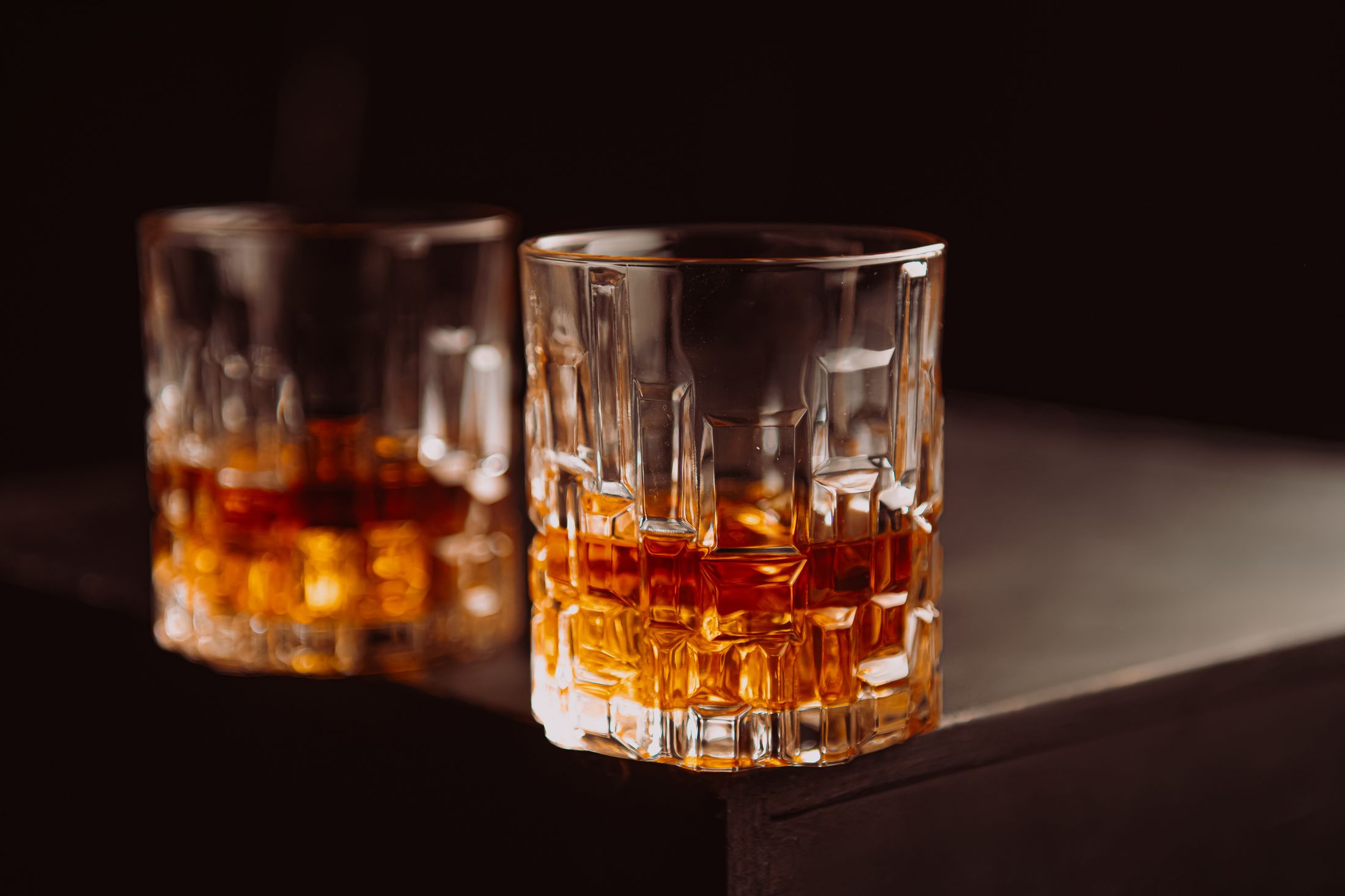 Two crystal glasses of bourbon catching warm light against a dark backdrop.