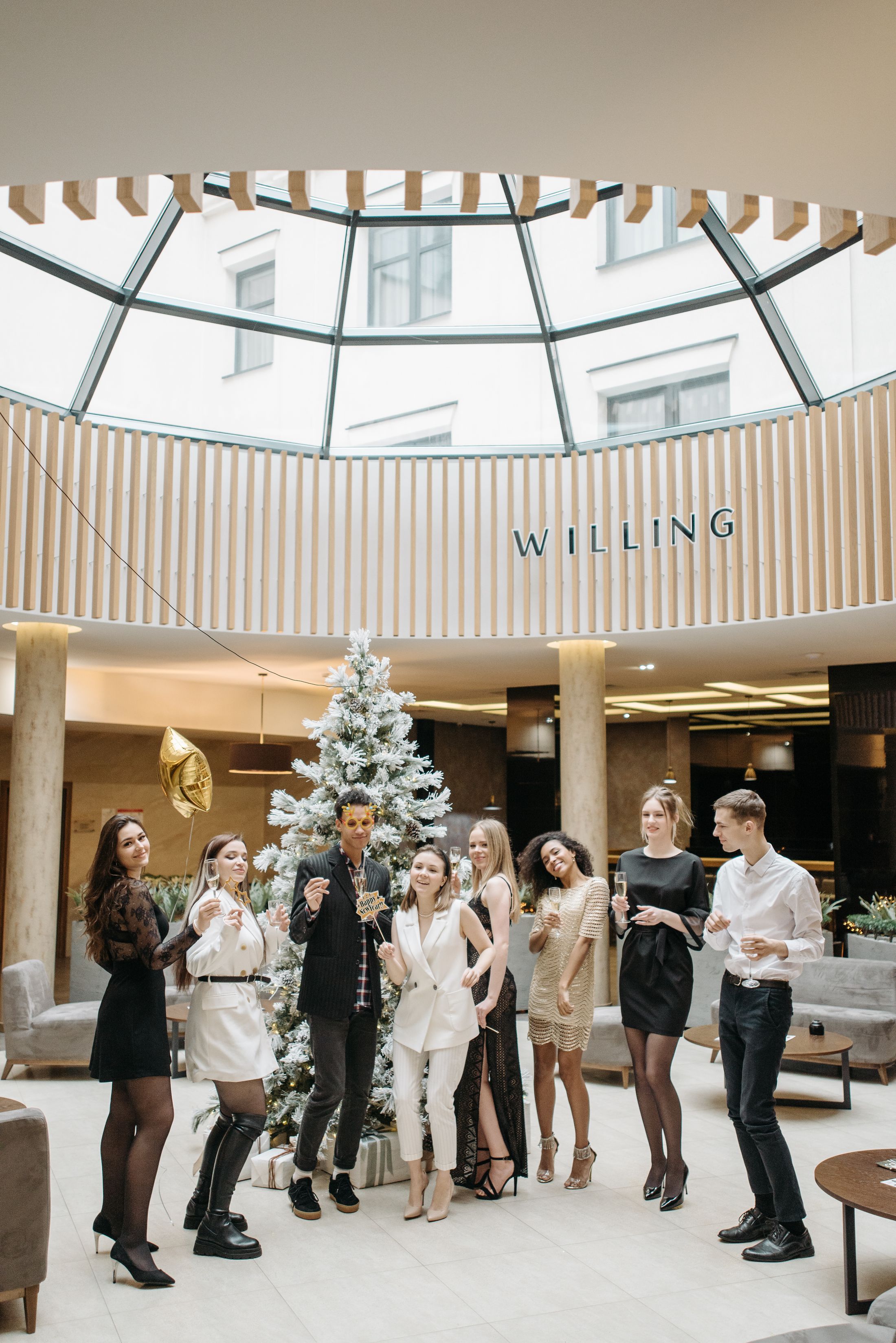 Guests in elegant evening attire celebrating at a corporate holiday party in a hotel atrium.