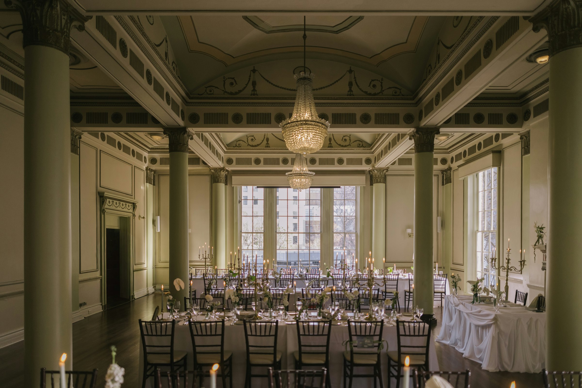 A candlelit ballroom reception with long tables set beneath a grand crystal chandelier.