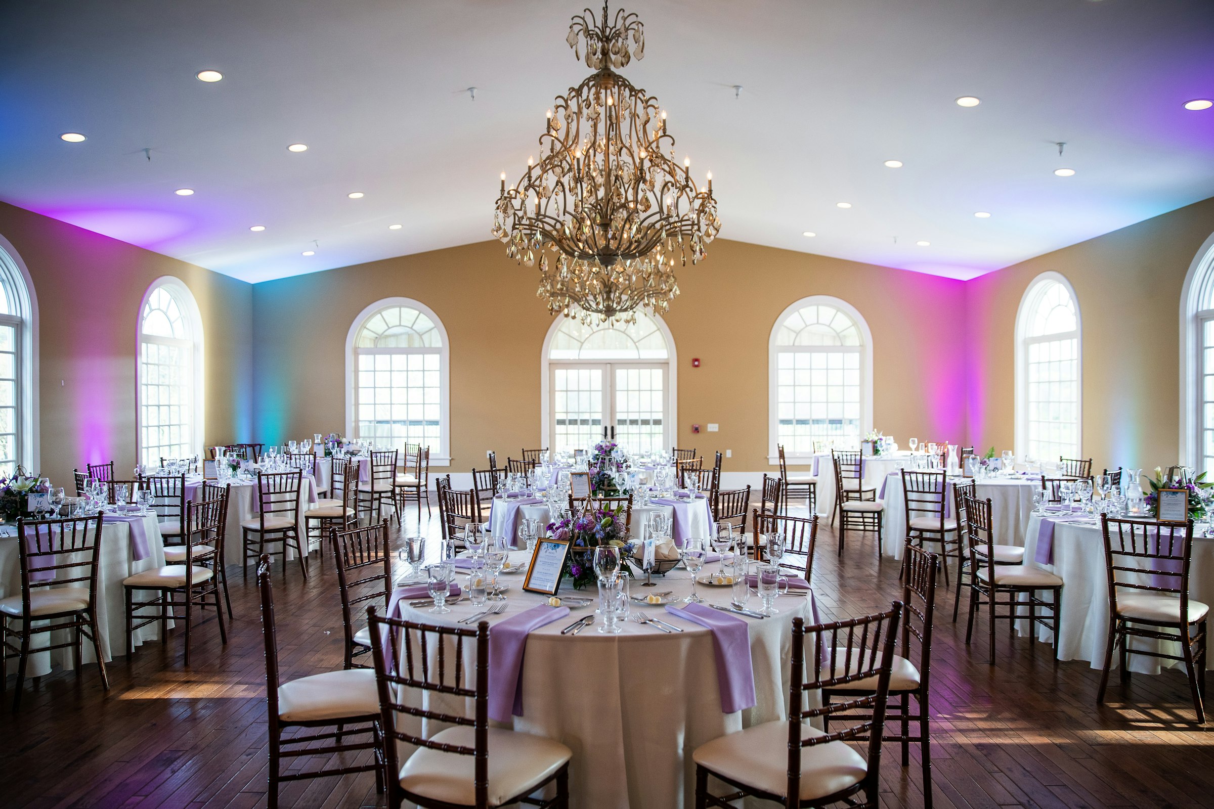 A grand banquet room set for a wedding reception beneath a crystal chandelier.